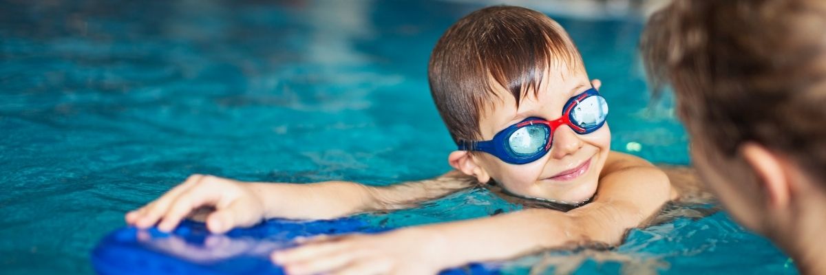 smiling boy with goggles on learning to swim with float